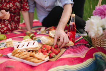 Close up of hand take strawberry on mini picnic outdoors. Man and woman eat outside