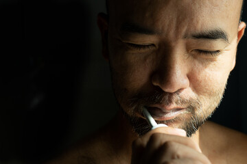 40s adult beard Asia man portrait cleaning teeth by electric toothbrush with morning light from window