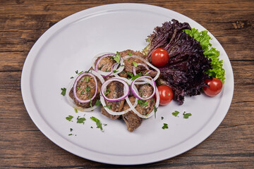 Lamb slices with herbs and tomatoes on a white plate on a wooden table.