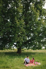 Happy couple sits has mini picnic near the big tree. Non alcoholic picnic