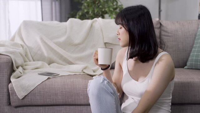 asian girl relaxing with tea in parlor noticed incoming call and pick it up. lovely chinese female answering phone from a good friend with cheerful mood.