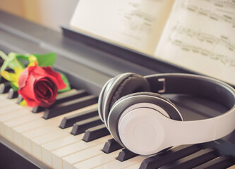 Obraz na płótnie Canvas Music concept.Music headphone on piano keyboard with red rose .