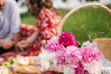 Close up of man and woman has non alcoholic picnic outdoors. Strawberry, lemonade, bread and other snacks. Beautiful peony flowers