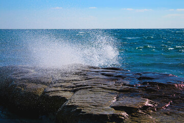 Rocky shore on the Mediterranean Sea, splashing waves breaking on stones.