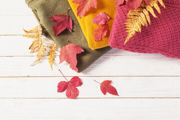 stack of sweaters with autumn leaves  on  white wooden table