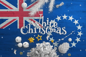 Fototapeta na wymiar Cook Islands flag on wooden table with White Christmas text. Christmas and new year background, celebration national concept with white decor.