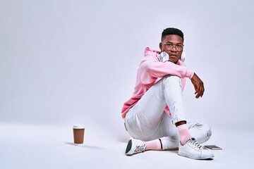 Lifestyle concept. Young African American man wearing a pink hoodie, white pants and pink socks...