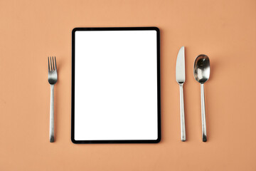 Tablet, fork, knife and spoon lying isolated on beige background, conceptual photography for food...