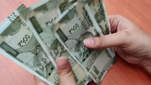 Hands counting new Rs 500 Rupees Indian Currency notes against a wooden bokeh background.