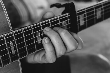 Fingers on guitar strings in black and white.