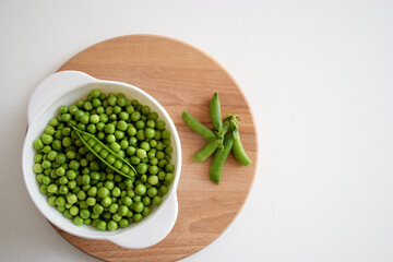 Fresh green peas and pods in white bowl on wooden cutting board. Healthy food, farm harvest concept.