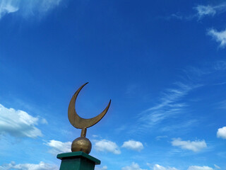 Fototapeta na wymiar Symbol of Islam and Islam is a crescent moon on a pillar. Against a blue sky with white clouds. Religion. Faith-inscrutable. Copy space for text. Background