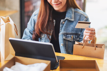 Closeup image of a young woman using tablet pc and credit card for online shopping with postal parcel box and shopping bags on the table