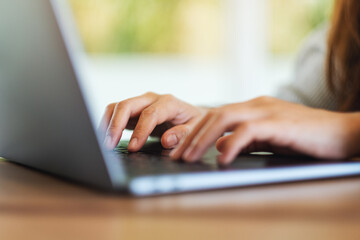 Closeup image of a young woman working and typing on laptop computer keyboard on wooden table