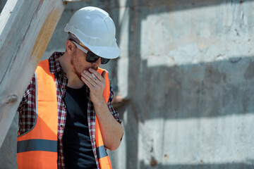 Construction site worker in a protective vest and hard hat, Smoking with a mobile phone in his hands