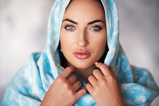Young woman of oriental appearance in a blue scarf. Beauty portrait of arabian or indian girl with perfect makeup and handmade accessories
