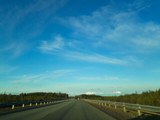 A road or highway leading to the horizon. View from the car window. Northern dim summer, blue sky with white clouds.