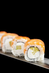 Japanese rolls and seafood sushi on a katana sword on a black background