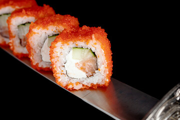Japanese rolls and seafood sushi on a katana sword on a black background
