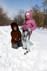 Fototapeta na wymiar a small smiling girl in snow-covered pants next to a smiling young woman squatting on the snow on a frosty day
