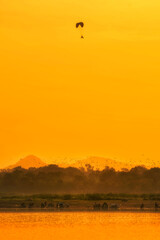 Silhouette of the Paramotor control flying through soft sunlight at sunset sky