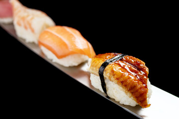 Japanese rolls and seafood sushi on a katana sword on a black background