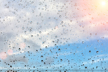 Raindrops on misted window glass against a blue sky. The sun is shining.