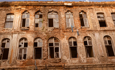 very old abandoned ruin building with many windows with broken glass on the front.