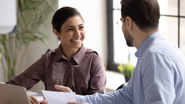 Smiling Indian businesswoman intern listening to mentor executive at meeting, staff training, manager consulting satisfied customer, diverse colleagues sharing ideas, discussing project strategy