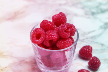 Raspberries in a glass on a light marble background