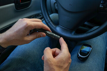 Lancet pen and glucometer in the hands of a man in a car. Diabetes concept.