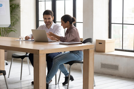Indian businesswoman mentor helping to new employee with corporate software, pointing at laptop screen, explaining task, giving instructions, friendly diverse colleagues working on project together