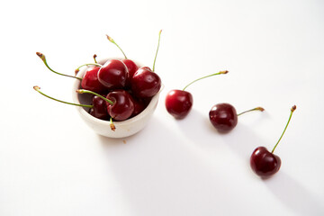 Fototapeta na wymiar Group of cherry in a small cup on a white background with shadows. Close-up. Top view.