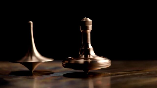 Two brass spinning top rotates on a copper plate on a black background. Time. Movie "Inception"