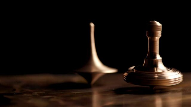Two brass spinning top rotates on a copper plate on a black background. Man rotates a brass spinning top on a copper plate. Time. Movie "Inception"