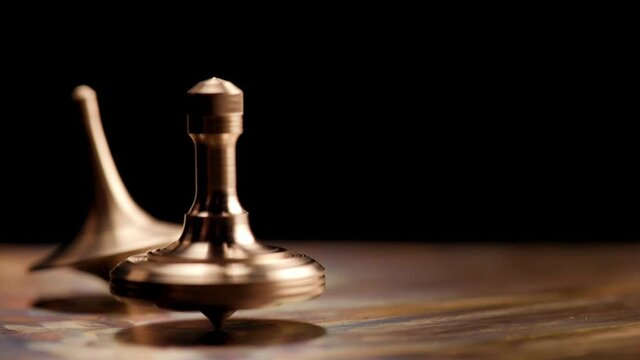Two brass spinning top rotates on a copper plate on a black background. Man rotates a brass spinning top on a copper plate. Time. Movie "Inception"
