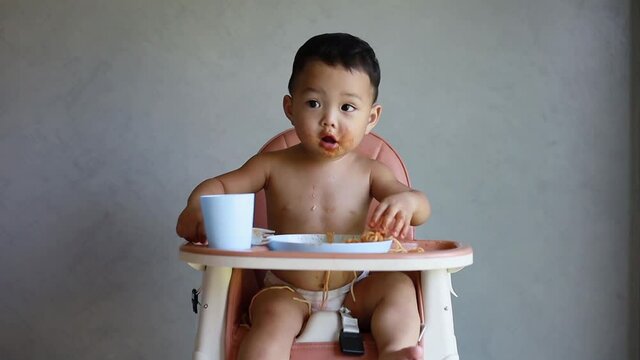 Asian boy eatting on high baby chair.
