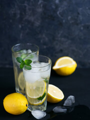 Two glasses of refreshing summer lemon mint lemonade with ice on the black table
