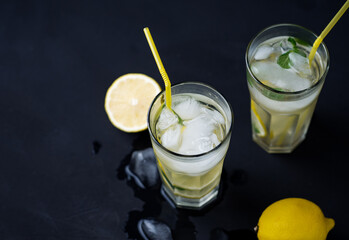 Two glasses of refreshing summer lemon mint lemonade with ice on the black table