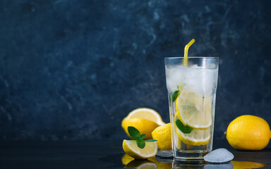 A glass of summer lemonade with lemon, mint, ice on a dark concrete table and copy space