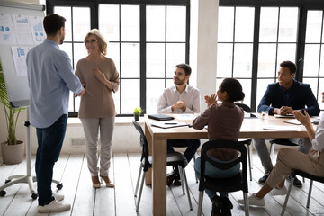 Confident businessman executive shaking middle aged businesswoman hand at corporate meeting, team...