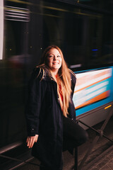 atractiva mujer pelirroja con pecas sonriente esperando el autobús en ropa informal de noche mirando a cámara