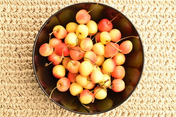 Yellow cherries in a black plate, close-up, on a straw mat.