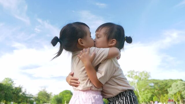 Two sibling girls are hugging and showing love to each other in the garden on a hot summer day.