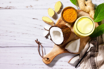 Cup of Healthy ayurvedic drink golden coconut milk turmeric iced latte with curcuma powder on kitchen table. Top view flat lay background. Copy space.