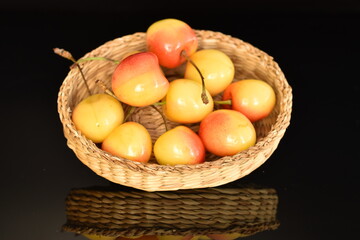 Yellow cherries in a straw plate, close-up, on a black background.