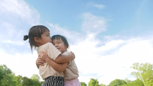 Two sibling girls are hugging and showing love to each other in the garden on a hot summer day.