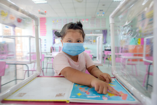 Asian school children wear medical masks, social distancing in classrooms and schools that are about to begin. There are plastic sheets between students studying together.