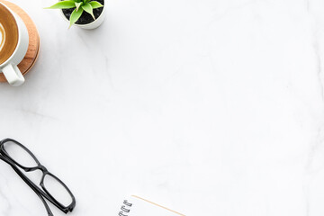 Minimal white marble office desk table with cup of latte coffee, notebook and supplies. Top view with copy space, flat lay.