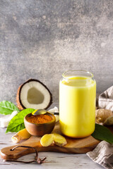 Cup of Healthy ayurvedic drink golden coconut milk turmeric iced latte with curcuma powder on kitchen table. Copy space.
